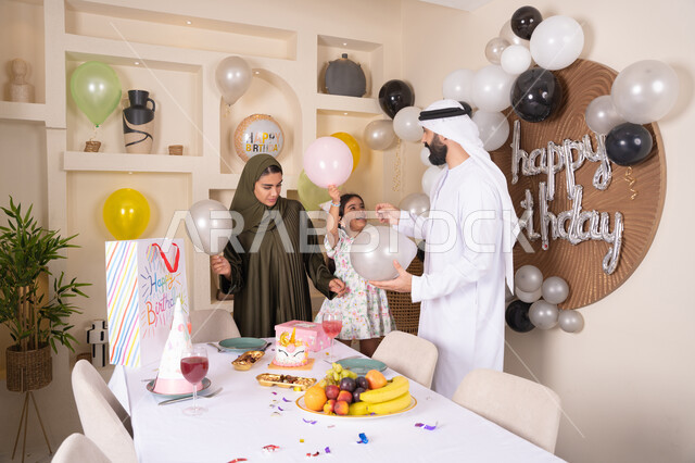 مشاركة وتقديم الهدايا بالمناسبات وأعياد الميلاد، إيماءات الفرح و السعادة، مشاعر الحب والحنان في اجتماع عائلي سعيد, أجواء أسرية مليئة بالألفة، بلالين وكعكة يوم الميلاد المزينة بالشموع،عائلة عربية خليجية إماراتية تقضي أوقات ممتعه في المنزل وتلعب بالبلالين