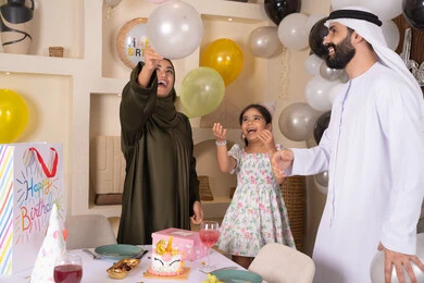 إيماءات الفرح و السعادة، مشاعر الحب والحنان في اجتماع عائلي سعيد, أجواء أسرية مليئة بالألفة، بلالين وكعكة يوم الميلاد المزينة بالشموع،عائلة عربية خليجية إماراتية تقضي أوقات ممتعه في المنزل وتلعب بالبلالين، مشاركة وتقديم الهدايا بالمناسبات وأعياد الميلاد