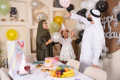 مشاعر الحب والحنان في اجتماع عائلي سعيد, أجواء أسرية مليئة بالألفة، بلالين وكعكة يوم الميلاد المزينة بالشموع،عائلة عربية خليجية إماراتية تقضي أوقات ممتعه في المنزل وتلعب بالبلالين، إيماءات الفرح و السعادة، مشاركة وتقديم الهدايا بالمناسبات وأعياد الميلاد