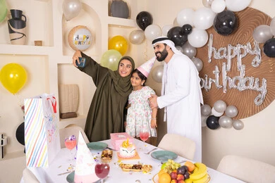 أسرة عربية خليجية اماراتية تقوم بالاحتفال بعيد الميلاد، ام عربية خليجية اماراتية تقوم بأخذ صورة تذكارية من خلال الجوال مع الكعكة المزينة بالشموع، مشاعر الحب والحنان في اجتماع عائلي سعيد, النظر الى الكاميرا بايماءات السرور والفرح، الاحتفال بالمناسبات والأعياد بأجواء عائلية سعيدة