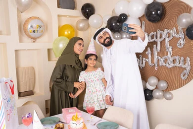 مشاعر الحب والحنان في اجتماع عائلي سعيد, النظر الى الكاميرا بايماءات السرور والفرح، الاحتفال بالمناسبات والأعياد بأجواء عائلية سعيدة, أسرة عربية خليجية اماراتية تقوم بالاحتفال بعيد الميلاد، رجل عربي خليجي اماراتي يقوم بأخذ صورة تذكارية من خلال الجوال مع الكعكة المزينة بالشموع