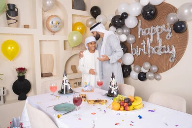 Enjoyment and entertainment with family members, gestures of happiness and pleasure, happy family holidays and occasions, an Arab Gulf Emirati father celebrating his son, the concept of gifting and appreciation, an Arab Gulf Emirati family spending fun times, birthday decorations