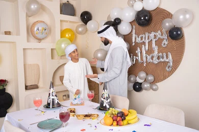 ايماءات السعادة و السرور ، أعياد ومناسبات عائلية سعيدة، اب عربي خليجي اماراتي يقوم بالاحتفال بابنه ، الاستمتاع و الترفيه مع افراد الاسره ،مفهوم الإهداء والتقدير، عائلة عربية خليجية اماراتيه تقضي اوقات ممتعه ، زينة أعياد الميلاد