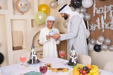 زينة أعياد الميلاد ، ايماءات السعادة و السرور ،مفهوم الإهداء والتقدير، أعياد ومناسبات عائلية سعيدة، اب عربي خليجي اماراتي يقوم بالاحتفال بابنه ، عائلة عربية خليجية اماراتيه تقضي اوقات ممتعه