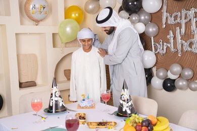 The concept of giving and appreciation, enjoyment and entertainment with family members, happy family holidays and occasions, an Arab Gulf Emirati father celebrating his son, an Arab Gulf Emirati family spending fun times, birthday decorations, gestures of happiness and pleasure