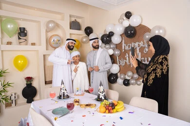 An Arab Gulf Emirati family celebrating their birthday, a woman taking a commemorative photo with her mobile phone, documenting happy moments, having fun and celebrating family occasions, birthday and event decorations, gestures of happiness and pleasure