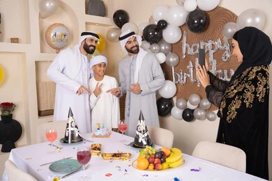 Having fun and celebrating family occasions, documenting happy moments, birthday and occasion decorations, an Arab Gulf Emirati family celebrating a birthday, a woman taking a souvenir photo with her mobile phone, gestures of happiness and pleasure