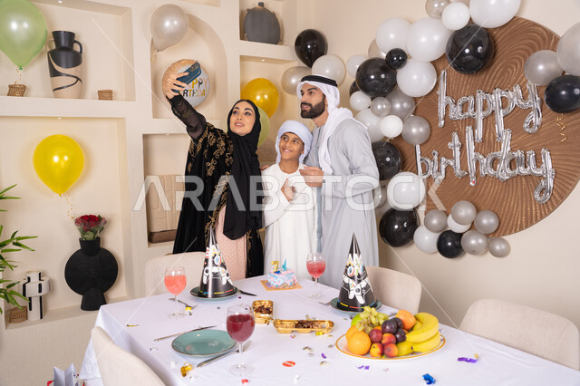الاحتفال بالمناسبات والأعياد بأجواء عائلية سعيدة, النظر الى الكاميرا بايماءات السرور والفرح ، ام عربية خليجية اماراتية تقوم بأخذ صورة تذكارية من خلال الجوال مع الكعكة المزينة بالشموع ،  أسرة عربية خليجية اماراتية تقوم بالاحتفال بعيد الميلاد، مشاعر الحب والحنان في اجتماع عائلي سعيد
