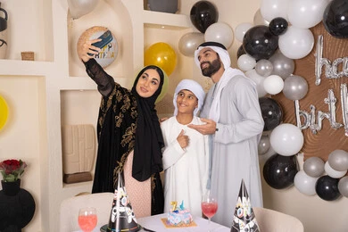 ام عربية خليجية اماراتية تقوم بأخذ صورة تذكارية من خلال الجوال مع الكعكة المزينة بالشموع ،  أسرة عربية خليجية اماراتية تقوم بالاحتفال بعيد الميلاد، مشاعر الحب والحنان في اجتماع عائلي سعيد, الاحتفال بالمناسبات والأعياد بأجواء عائلية سعيدة, النظر الى الكاميرا بايماءات السرور والفرح