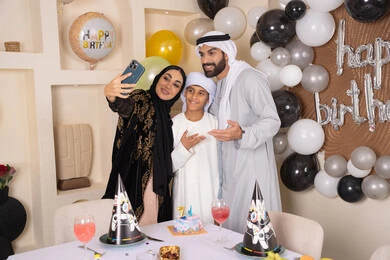 أسرة عربية خليجية اماراتية تقوم بالاحتفال بعيد الميلاد، مشاعر الحب والحنان في اجتماع عائلي سعيد, ام عربية خليجية اماراتية تقوم بأخذ صورة تذكارية من خلال الجوال مع الكعكة المزينة بالشموع ، الاحتفال بالمناسبات والأعياد بأجواء عائلية سعيدة, النظر الى الكاميرا بايماءات السرور والفرح