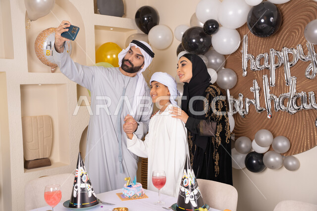 الاحتفال بالمناسبات والأعياد بأجواء عائلية سعيدة, النظر الى الكاميرا بايماءات السرور والفرح ، مشاعر الحب والحنان في اجتماع عائلي سعيد,  أسرة عربية خليجية اماراتية تقوم بالاحتفال بعيد الميلاد، رجل عربي خليجي اماراتي يقوم بأخذ صورة تذكارية من خلال الجوال مع الكعكة المزينة بالشموع