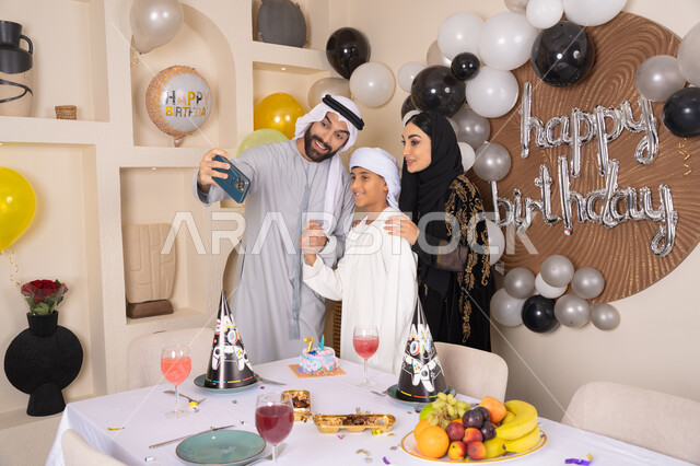 النظر الى الكاميرا بايماءات السرور والفرح ، مشاعر الحب والحنان في اجتماع عائلي سعيد,  أسرة عربية خليجية اماراتية تقوم بالاحتفال بعيد الميلاد، الاحتفال بالمناسبات والأعياد بأجواء عائلية سعيدة, رجل عربي خليجي اماراتي يقوم بأخذ صورة تذكارية من خلال الجوال مع الكعكة المزينة بالشموع