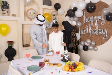 مشاعر الحب والحنان في اجتماع عائلي سعيد، أجواء أسرية مليئة بالألفة، بلالين وكعكة يوم الميلاد المزينة بالشموع، مشاركة وتقديم الهدايا بالمناسبات وأعياد الميلاد ، إيماءات الفرح و السعادة، عائلة عربية خليجية إماراتية تقضي أوقات ممتعه في المنزل