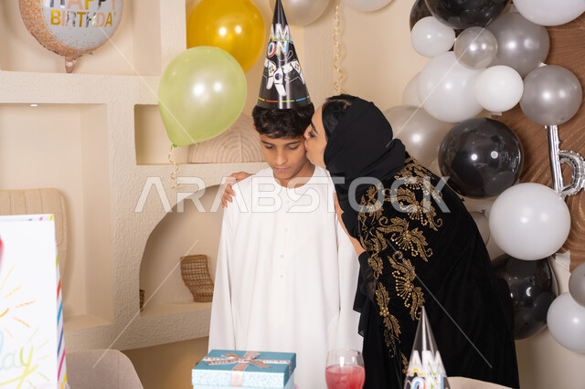 تعزيز روابط الامومه والحنان ، الاحتفال بأعياد الميلاد ضمن أجواء عائلية، تعليق الزينة والبالونات الملونة، ام عربيه خليجيه اماراتية ترتدي العباءه والحجاب ، تقوم بالاحتفال و تقبيل ابنها بايماءات السعادة و السرور