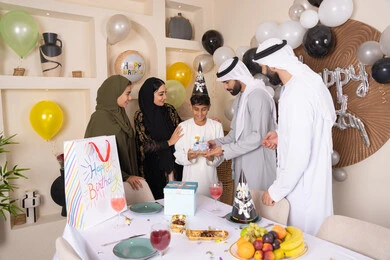 أجواء أسرية مليئة بالألفة، بلالين وكعكة يوم الميلاد المزينة بالشموع، مشاركة وتقديم الهدايا بالمناسبات وأعياد الميلاد ، إيماءات الفرح و السعادة، مشاعر الحب والحنان في اجتماع عائلي سعيد، عائلة عربية خليجية إماراتية تقضي أوقات ممتعه في المنزل