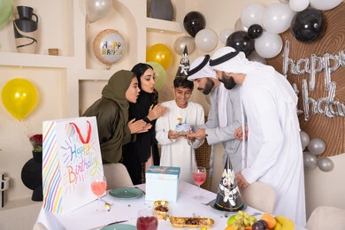 مشاعر الحب والحنان في اجتماع عائلي سعيد، عائلة عربية خليجية إماراتية تقضي أوقات ممتعه في المنزل، مشاركة وتقديم الهدايا بالمناسبات وأعياد الميلاد ، إيماءات الفرح و السعادة، بلالين وكعكة يوم الميلاد المزينة بالشموع، أجواء أسرية مليئة بالألفة