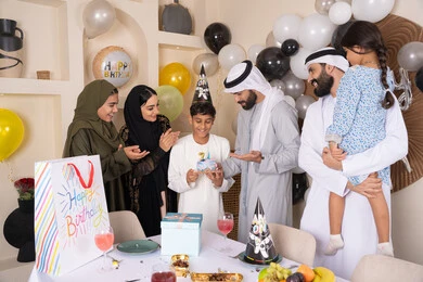 عائلة عربية خليجية إماراتية تقضي أوقات ممتعه في المنزل، مشاركة وتقديم الهدايا بالمناسبات وأعياد الميلاد ، إيماءات الفرح و السعادة، بلالين وكعكة يوم الميلاد المزينة بالشموع، أجواء أسرية مليئة بالألفة،  مشاعر الحب والحنان في اجتماع عائلي سعيد