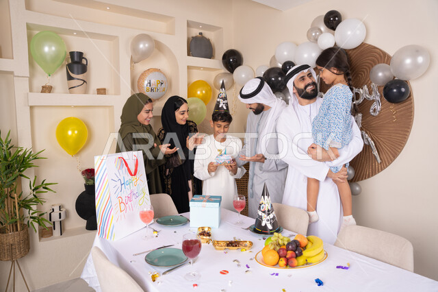 إيماءات الفرح و السعادة، بلالين وكعكة يوم الميلاد المزينة بالشموع، أجواء أسرية مليئة بالألفة،  مشاعر الحب والحنان في اجتماع عائلي سعيد,عائلة عربية خليجية إماراتية تقضي أوقات ممتعه في المنزل، مشاركة وتقديم الهدايا بالمناسبات وأعياد الميلاد