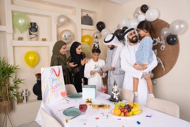 إيماءات الفرح و السعادة، بلالين وكعكة يوم الميلاد المزينة بالشموع، أجواء أسرية مليئة بالألفة،  مشاعر الحب والحنان في اجتماع عائلي سعيد,عائلة عربية خليجية إماراتية تقضي أوقات ممتعه في المنزل، مشاركة وتقديم الهدايا بالمناسبات وأعياد الميلاد