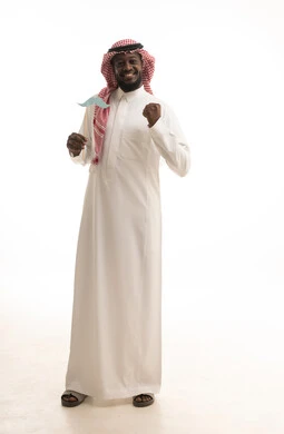 Gestures of victory and triumph, promoting physical well-being for men, International Men's Day on November 19, attention to external appearance, celebrating global occasions, a portrait of an Arab Gulf Saudi man wearing traditional attire and a ghutrah holding a wooden stick with paper cutouts shaped like a mustache, full body length, white background.