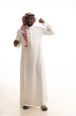 Maintaining the strength and fitness of males, celebrating global occasions, preserving fitness and muscle strength, International Men's Day on November 19, a portrait of an Arab Gulf Saudi man wearing traditional attire and a ghutrah holding a paper cutout in the shape of a mustache, full body length, white background.