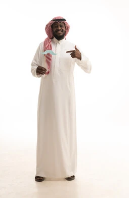 الحفاظ على اللياقة والصحة الجسدية للذكور، مفهوم القوة والرجولة، إيماءات الثقة والاعتزاز بالنفس، بورتريه لرجل عربي خليجي سعودي يرتدي الثوب التقليدي والشماغ يضع في جيبه قصاصة ورقية على شكل شارب ويقوم بالإشارة اليها، صورة لكامل الجسم، خلفية بيضاء