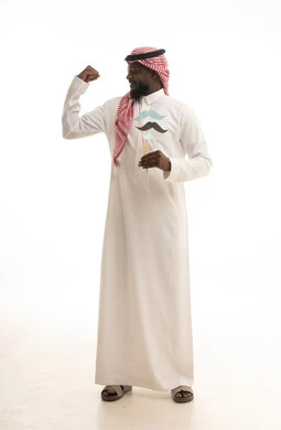 الإحتفال بالمناسبات العالمية، الإهتمام بصحة الرجال، المحافظة على اللياقة والقوة العضلية، اليوم العالمي للرجل 19 نوفمبر، بورتريه لرجل عربي خليجي سعودي يرتدي الثوب التقليدي والشماغ يمسك بيدية قصاصة ورقية على شكل شارب، الطول الكامل للجسم، خلفية بيضاء