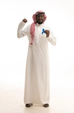 Gestures of interaction and integration, a feeling of strength and success, a portrait of a young Arab Gulf Saudi man wearing traditional attire holding a blue ribbon for disease awareness, full-body, white background.