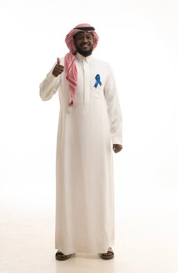Raising the hand with gestures of approval and acceptance, awareness and guidance campaigns not to neglect health, a portrait of an Arab Gulf Saudi man wearing traditional attire and a ghutrah holding a blue ribbon in his hand to indicate prostate cancer, the importance of early detection of cancers, full body length, white background.