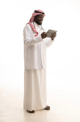 وصف العلاج والتوعيه الطبيه والتثقيفيه، وصف الحالة المرضية وتقديم الاستشارات الطبية، متابعة السجل الطبي الالكتروني الخاص بالمريض، بورتريه لطبيب عربي خليجي سعودي يرتدي المعطف والسماعة الطبية يحمل بيده جهاز التابلت، صوره الجسم الكامل، خلفية بيضاء