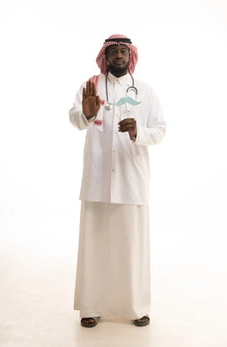 سنوية اليوم العالمي للرجل، ايماءات يدين تدل على الحذر وترك مسافة للحماية من العدوى، مفهوم الطب والرعاية الصحية، بورتريه لطبيب عربي خليجي سعودي يرتدي  الشماغ و المعطف الطبي والسماعات الطبية يحمل بيده عود خشبي مع قصاصة ورقية على شكل شارب، الطول الكامل للجسم، خلفية بيضاء