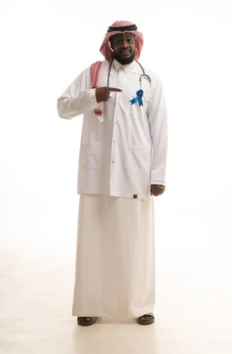 The concept of medicine and healthcare, early detection of diseases and following preventive methods, a portrait of an Arab Gulf Saudi doctor wearing a ghutrah and a lab coat with a stethoscope, pointing with his index finger to the awareness logo for prostate cancer, full body length, white background.