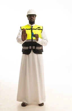 An open hand raised to warn against ignoring disease detection, awareness and guidance campaigns for early disease detection, a portrait of an Arab Gulf Saudi engineer wearing traditional attire, a helmet, and a safety vest holding a blue ribbon for prostate cancer awareness, standing upright with gestures of determination and seriousness, white background.