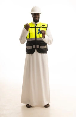 رفع اليد بإيماءات الفوز و الانتصار، الحفاظ على الصحة الجسدية، حملات الإرشاد والتنبيه للكشف المبكر عن سرطان البروستات،بورتريه لمهندس عربي خليجي سعودي يرتدي الثوب التقليدي و الخوذة وسترة الحماية يحمل شريط أزرق للتوعية بالأمراض، الجسم بالطول الكامل، خلفية بيضاء