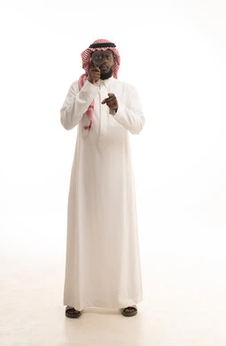 Referring to something, the concept of clarifying the image, examination and exploration and close-up vision, a portrait of a Gulf Arab Saudi man wearing traditional attire and a shemagh looking through a magnifying glass, scrutiny and focus using optical tools, a full-body image, white background.