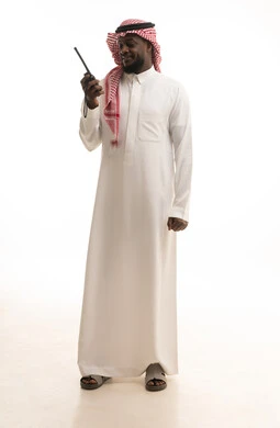 الإستجابة لحالات الطوارئ، المتابعة والإشراف على خطط العمل، بورتريه لرجل عربي خليجي سعودي يرتدي الثوب التقليدي والشماغ يقوم باستخدم جهاز الارسال والاستقبال اللاسلكي، مفهوم ادارة المشاريع عن بعد، صورة لكامل الجسم، خلفية بيضاء