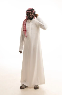 استخدام سماعات الرأس والتقنيات المتطورة في العمل، الرد على الاستفسارات والاستعلامات, بورتريه لرجل عربي خليجي سعودي يرتدي الشماغ والثوب التقليدي يضع الهيدفون يعمل في قسم خدمة العملاء، التواصل مع الزبائن لحل المشكلات والشكاوي، صورة الجسم بالكامل، خلفية بيضاء