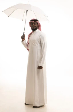 النظر إلى الكاميرا بإيماءات السعادة والسرور, التظلل من أشعة الشمس, الحماية من الأمطار في الشتاء، بورتريه لرجل عربي سعودي يرتدي الزي التقليدي و الشماغ  بيده مظلة بيضاء, الجسم بالطول الكامل, خلفية بيضاء