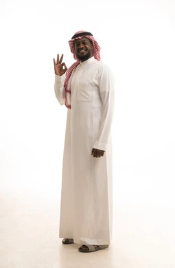 النظر إلى الكاميرا بإشارات الموافقه، حركات الاعجاب والقبول, الشعور بالرضا و السعادة, بورتريه مقرب لرجل عربي خليجي سعودي مبتسم يرتدي  الثوب التقليدي و الشماغ يرفع يده للأعلى بإيماءات علامة الجودة و السرور, الجسم بالطول الكامل، خلفية بيضاء