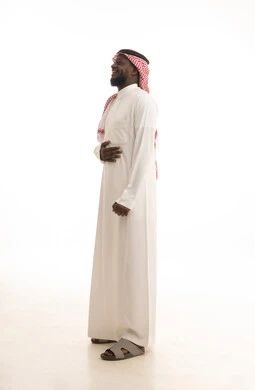 ايماءات البهجة والسرور الشديد، الشعور بالفرح والسعادة، بورتريه لرجل عربي خليجي سعودي اسمر يرتدي الثوب الأبيض و الشماغ  يضع يده على بطنه بتعابير الضحك الهستيري، الجسم بالطول الكامل، خلفية بيضاء