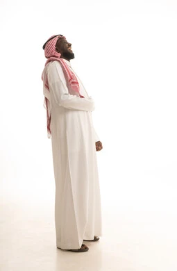 الشعور بالفرح والسعادة، بورتريه لرجل عربي خليجي سعودي اسمر يرتدي الثوب الأبيض و الشماغ  يضع يده على بطنه بتعابير الضحك الهستيري,ايماءات البهجة والسرور الشديد، الجسم بالطول الكامل، خلفية بيضاء