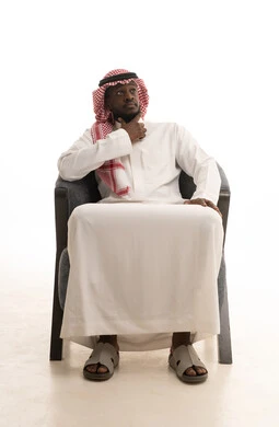التفكير في شيء هام، التأمل وشرود الذهن، بورترية لرجل عربي خليجي سعودي يرتدي الثوب التقليدي والشماغ يجلس على الكرسي يضع يده على ذقنه وينظر الى شيء، خلفية بيضاء