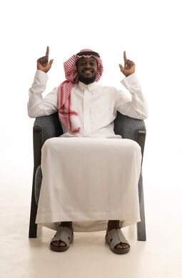 الاشارة إلى شيء ما،  تعابير التحديد والتأكيد، اشارات تحدد هذا المكان (هنا)، بورتريه لرجل عربي خليجي سعودي يرتدي الثوب التقليدي و الشماغ يجلس على كرسي و يشير بيدية الى الاعلى ، خلفية بيضاء