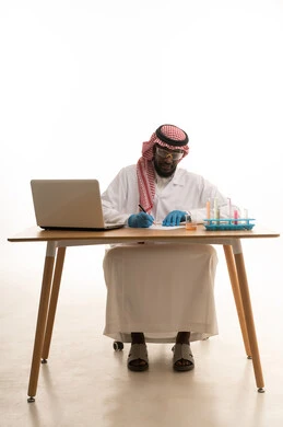 Taking notes and results, sitting in the chemistry lab, a portrait of an Arab Gulf Saudi doctor wearing a white lab coat and a ghutrah sitting behind a table in front of a laptop, using test tubes to conduct experiments in the lab, chemical reactions, research and development, the concept of biochemistry, white background.