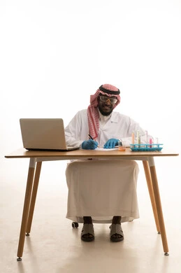 Sitting in the chemistry lab, taking notes and results, a portrait of an Arab Gulf Saudi doctor wearing a white lab coat and a ghutrah sitting behind a table in front of a laptop, using test tubes to conduct experiments in the lab, chemical reactions, research and development, the concept of biochemistry, white background.