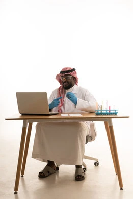 Conducting studies and chemical reactions, research and development, and advancements in biotechnology, using test tubes to conduct experiments and scientific research, a portrait of an Arab Gulf Saudi man wearing traditional thobe and ghutrah sitting behind a table in front of a laptop examining analytical samples, white background. Conducting studies and chemical reactions, research and development, and advancements in biotechnology, using test tubes to conduct experiments and scientific research, a portrait of an Arab Gulf Saudi man wearing traditional thobe and ghutrah sitting behind a table in front of a laptop examining analytical samples, white background.