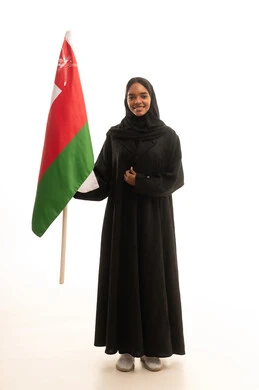 النظر بتعابير الفخر والاعتزاز، الاحتفال باليوم الوطني العماني 18نوفمبر, إحياء ذكرى استقلال الدولة 1650 م، المشاركة بالاعياد والمناسبات الوطنية، بورتريه لشابة عربية خليجية عمانية ترتدي العباءة والحجاب تحمل بيدها علم سلطنة عمان، صورة الجسم بالكامل، خلفية بيضاء