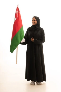 المشاركة بالاعياد والمناسبات الوطنية، الاحتفال باليوم الوطني العماني 18نوفمبر, إحياء ذكرى استقلال الدولة 1650 م،بورتريه لشابة عربية خليجية عمانية ترتدي العباءة والحجاب تحمل بيدها علم سلطنة عمان، النظر بتعابير الفخر والاعتزاز، صورة الجسم بالكامل، خلفية بيضاء