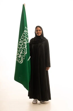 بورتريه لامرأة عربية خليجية سعودية  ترتدي العباءة والحجاب تحمل علم المملكة العربية السعودية، مفهوم حب الوطن والانتماء اليه، الإحتفال باليوم الوطني ، يوم العلم السعودي ،خلفية بيضاء