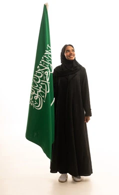 يوم العلم السعودي ، الإحتفال باليوم الوطني ، مفهوم حب الوطن والانتماء اليه، بورتريه لامرأة عربية خليجية سعودية  ترتدي العباءة والحجاب تحمل علم المملكة العربية السعودية، خلفية بيضاء